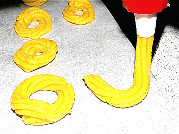 pipe bag forming spritz cookies on the baking pan
